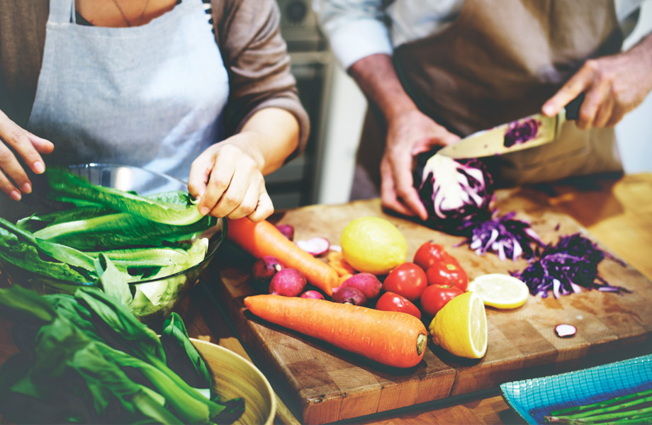 People cutting carrots, cabbage, and other vegetables on a cutting board