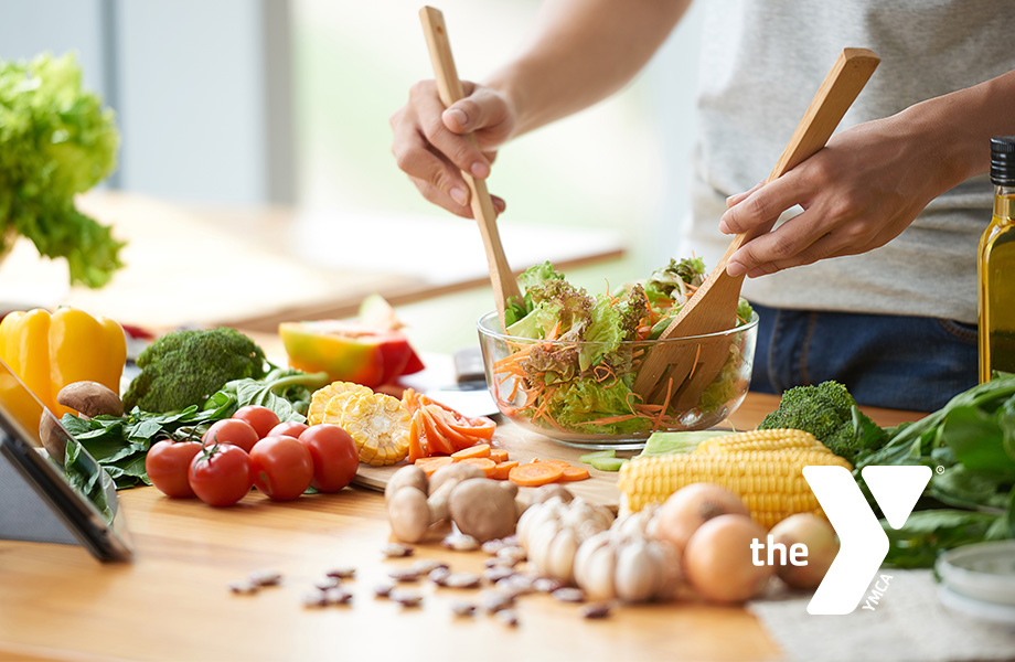 Two hands mixing a salad of green vegetables and peppers with utensils