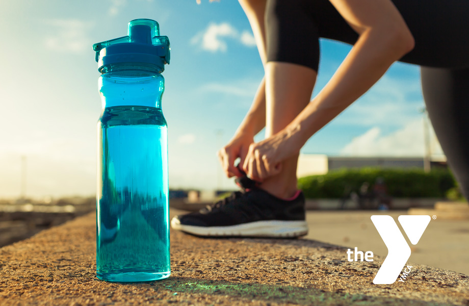 Woman adjusting running shoe behind full water bottle