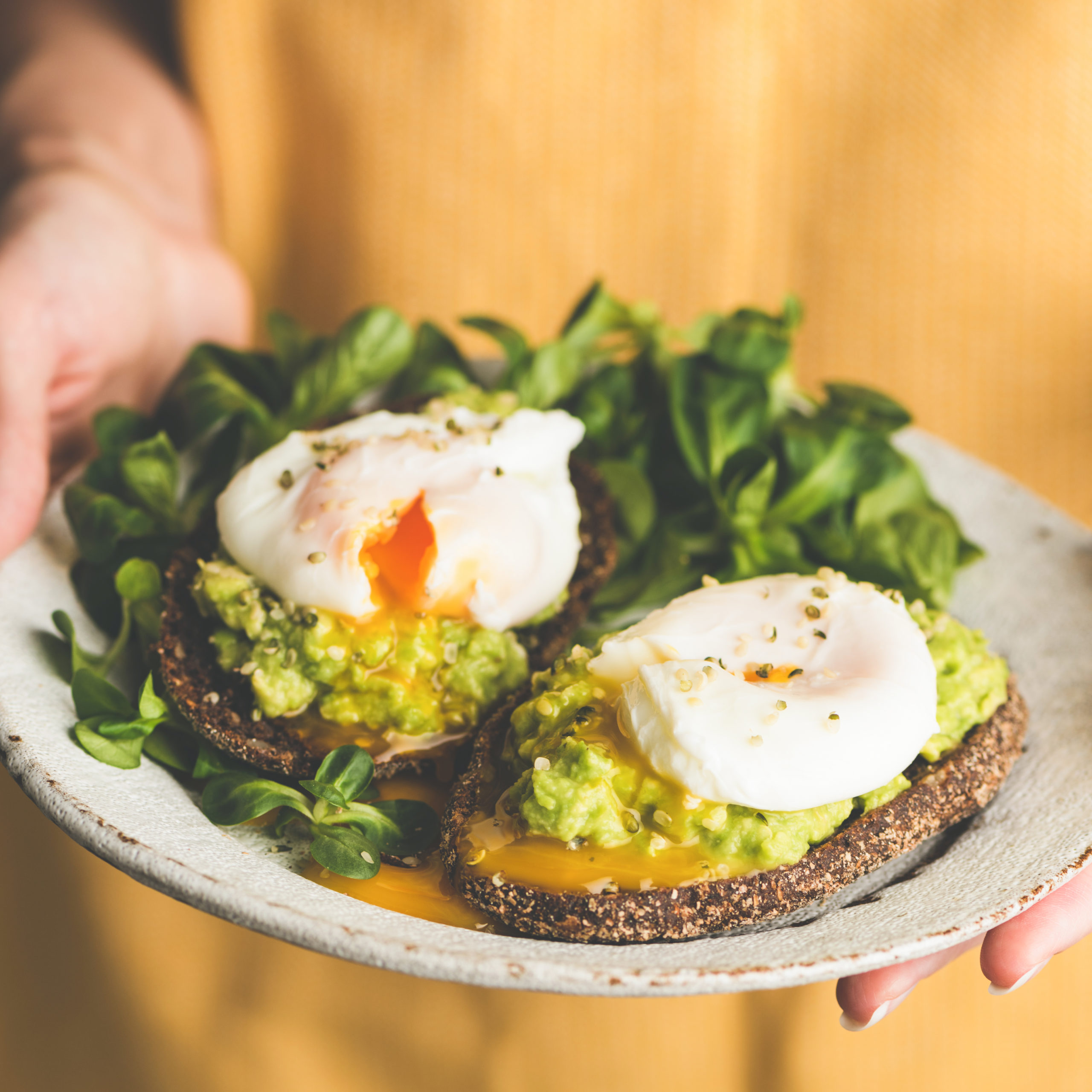 Avocado toast with poached egg in a white plate being held by a person