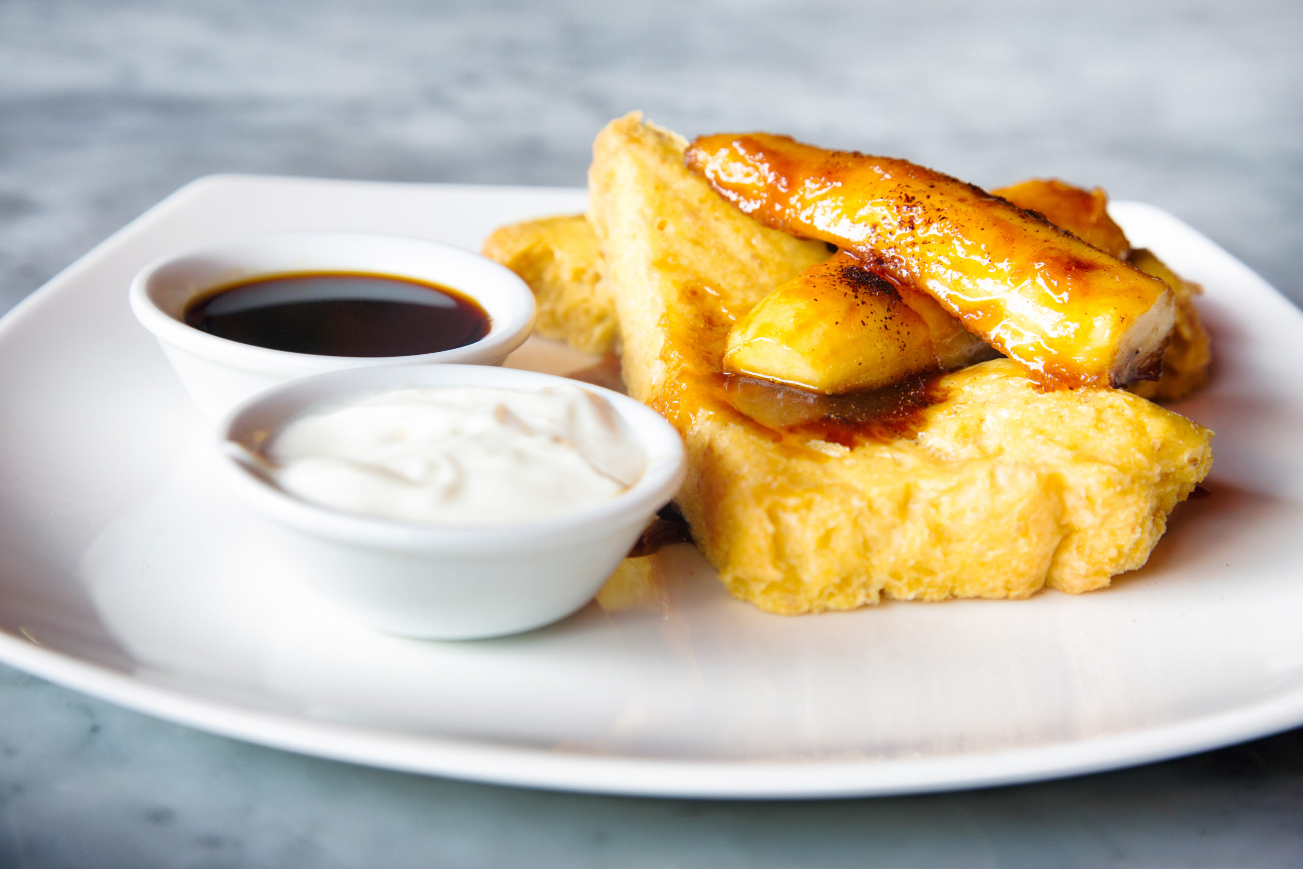 French toast with caramelized bananas on a white plate with creme and syrup
