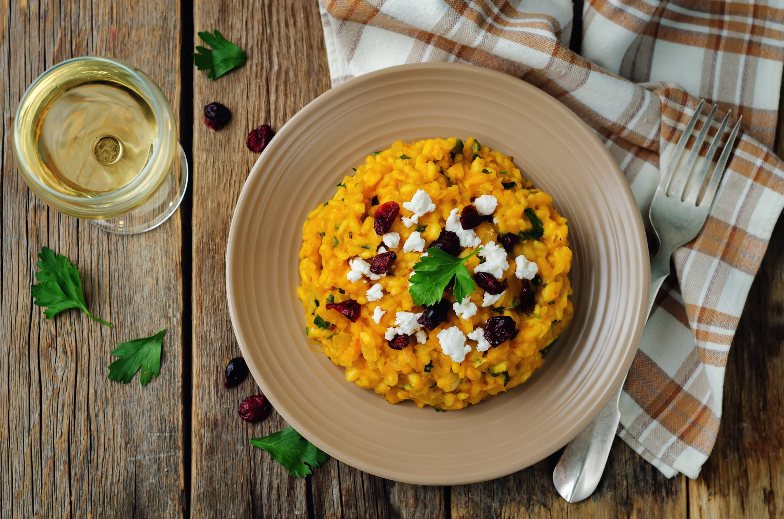 Pumpkin and goat cheese risotto in plate on a wooden table with a brown plaid tea towel