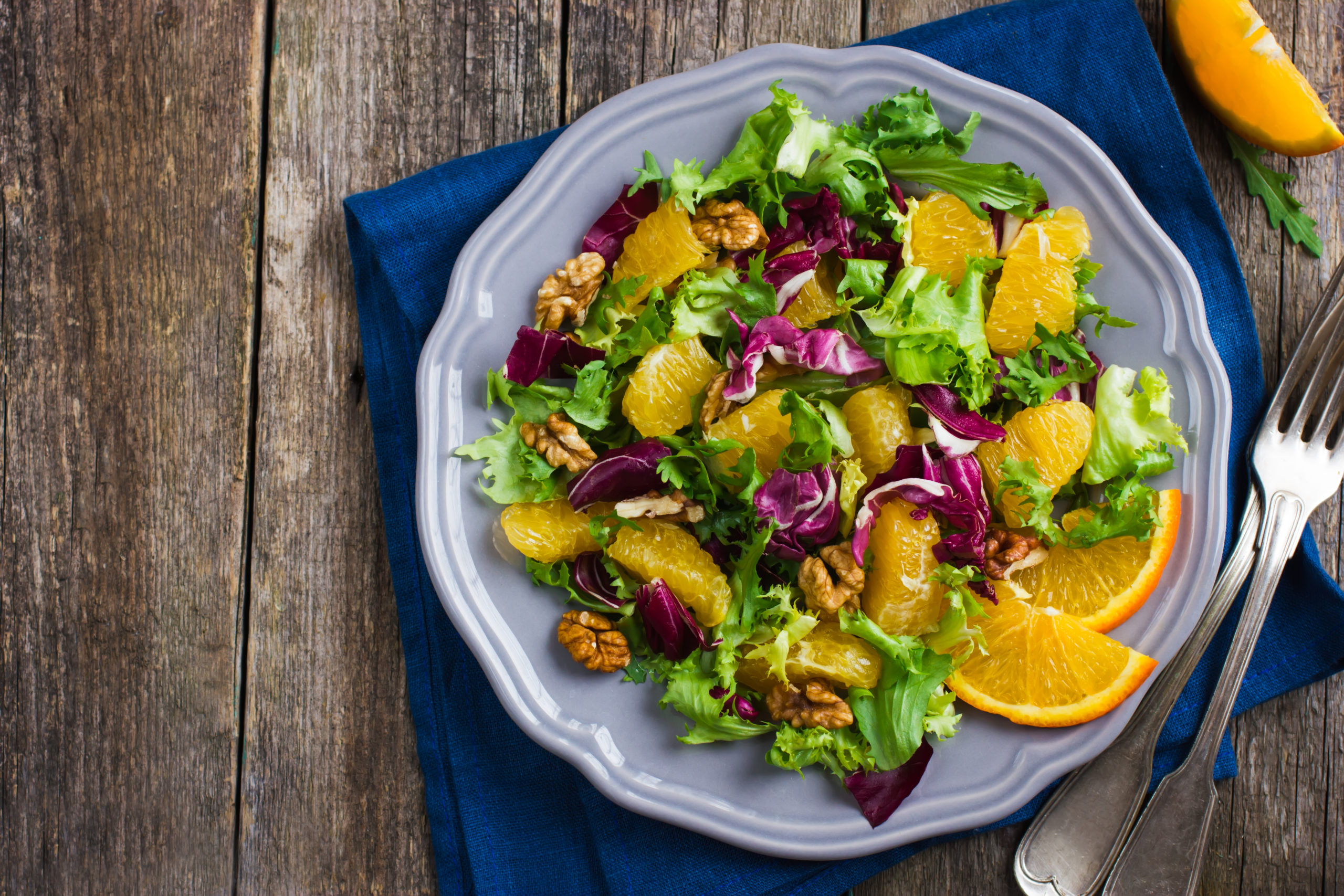 Baby Greens Salad with Orange Citronette on a plate with a blue napkin and fork beside it