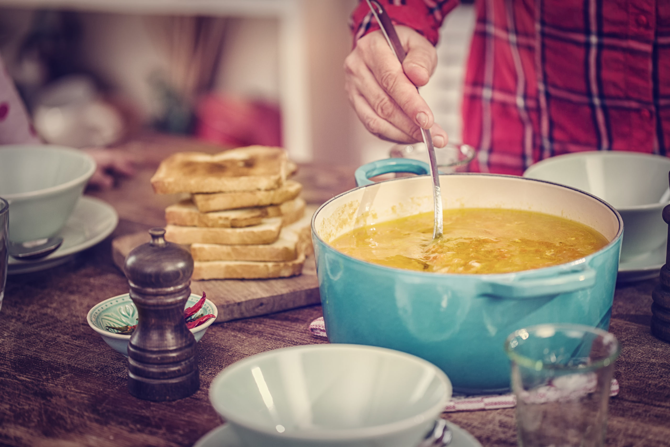 Woman making chicken soup in a pot next to grilled cheese sandwiches