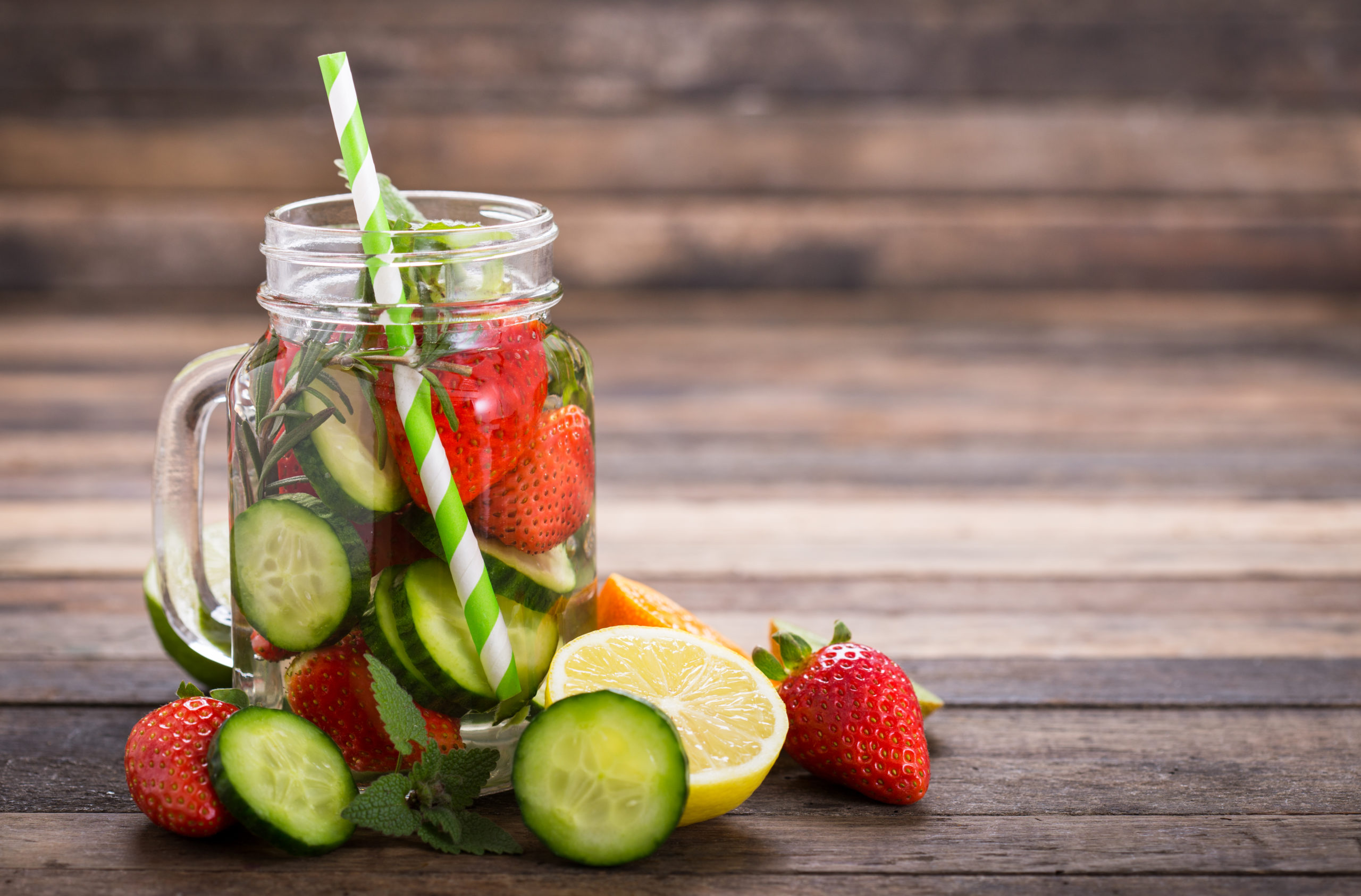 Cucumber lemon water in mason jar glass with paper straw on wooden surface