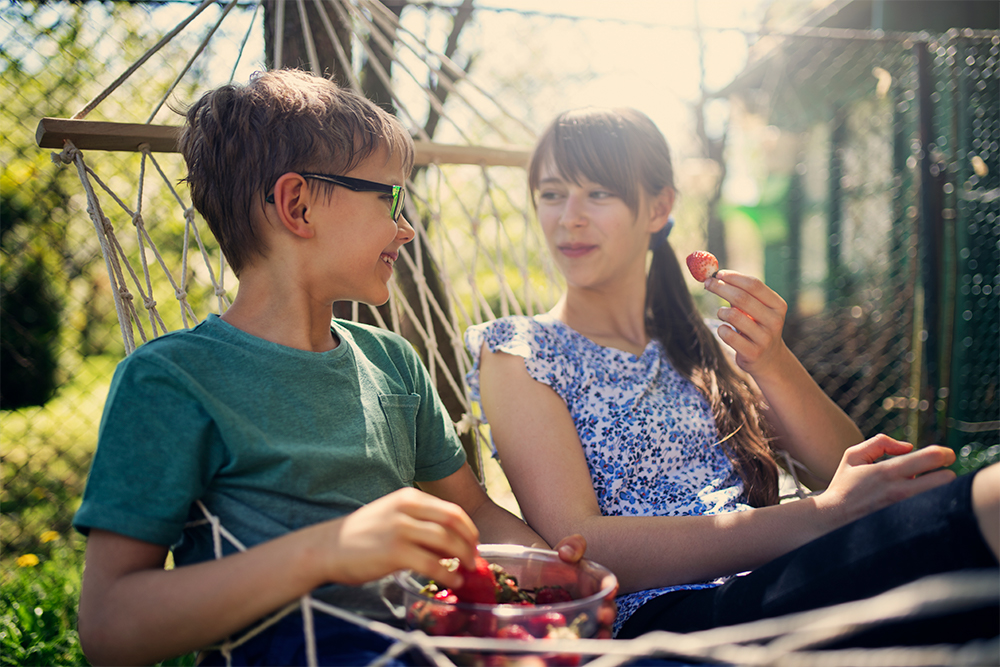 Two people sitting in a hammock eating strawberries
