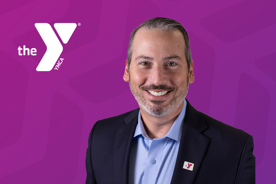 Headshot of Dan Saginario with a purple chevron background and the white Y logo