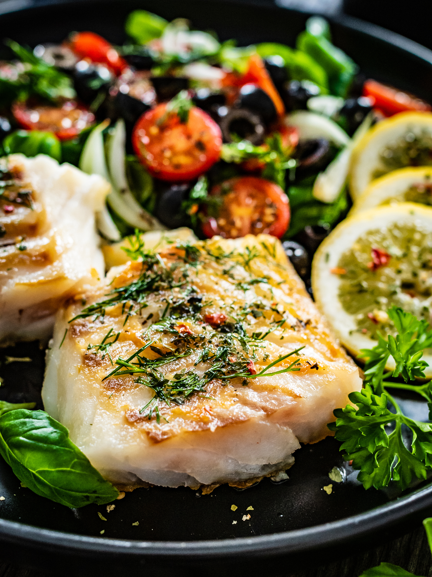 Baked cod on a plate on top of greens with lemon and tomatoes