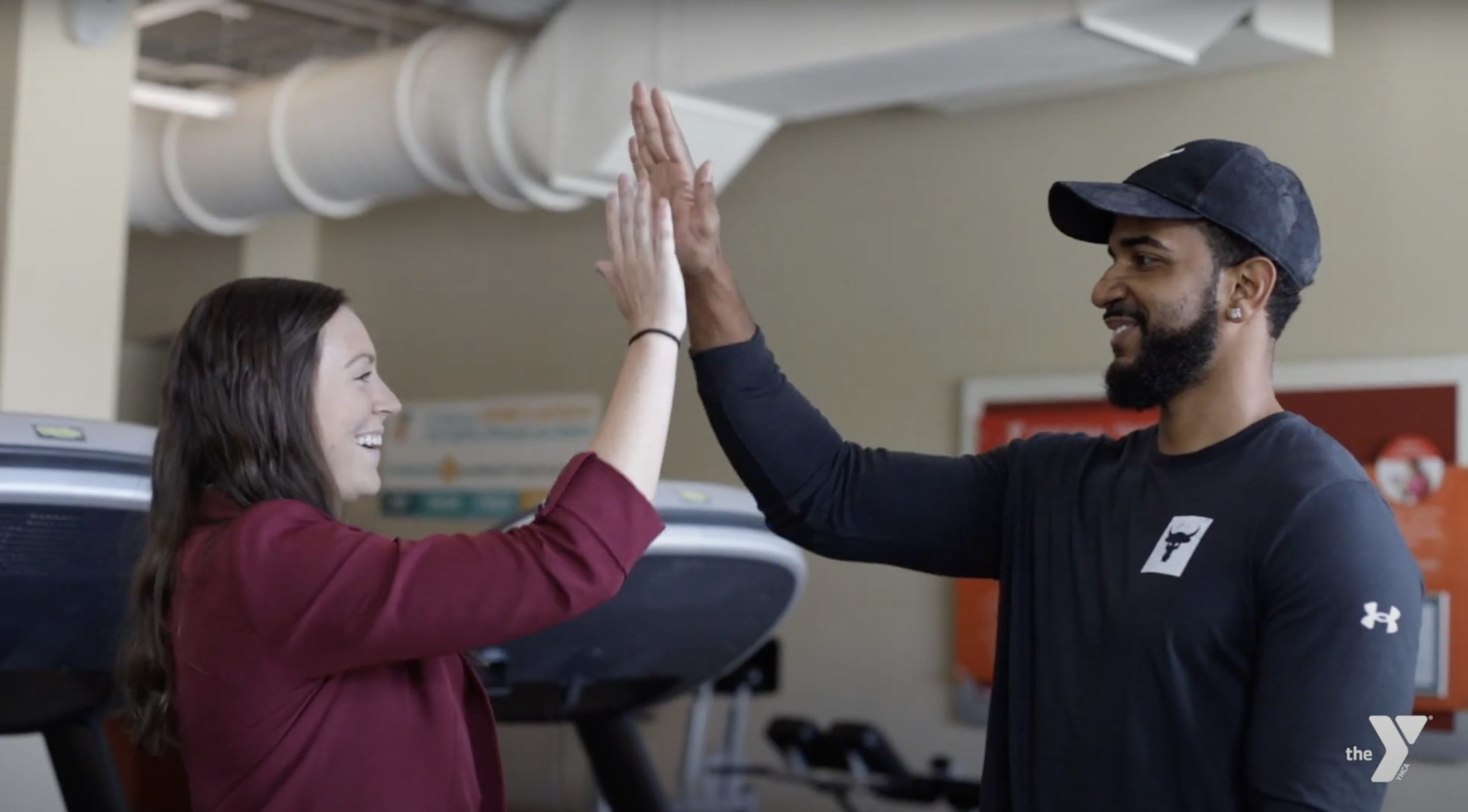 Image of Brittany Tilley high-fiving a Y Team member in front of fitness equipment