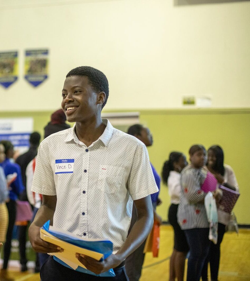 Teen smiling at college and career fair while holding folder and resume.