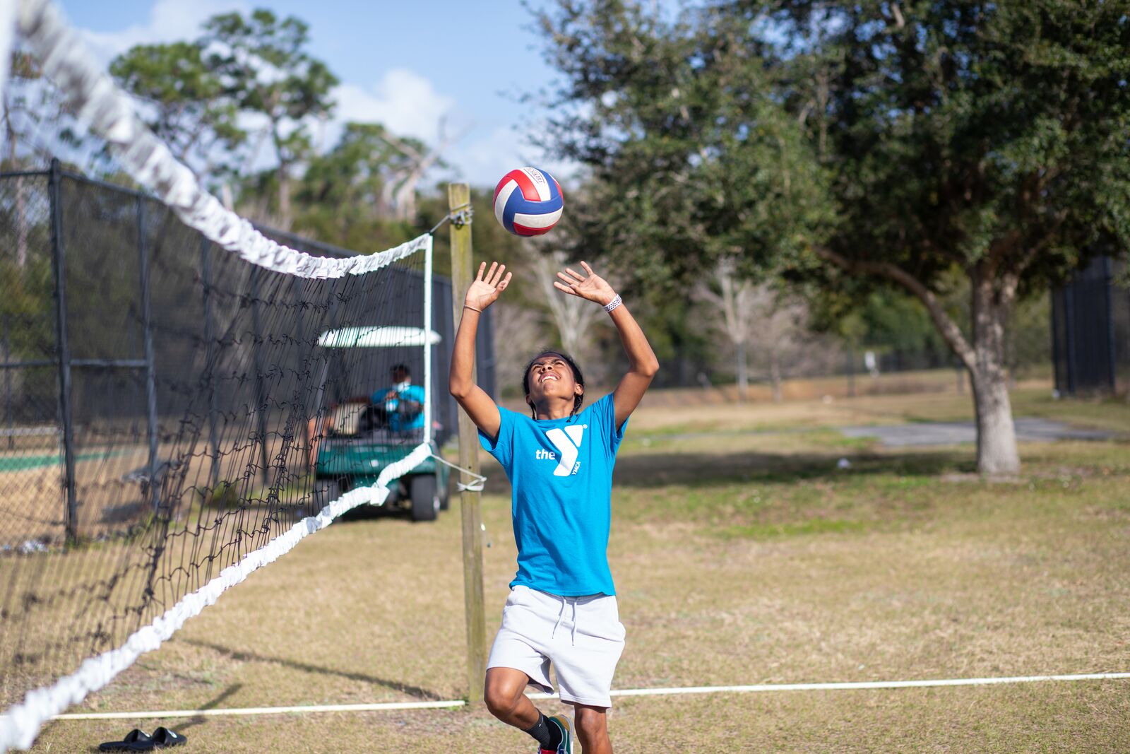 Teenager setting a volleyball at an outdoor volleyball court while wearing a Y t-shirt