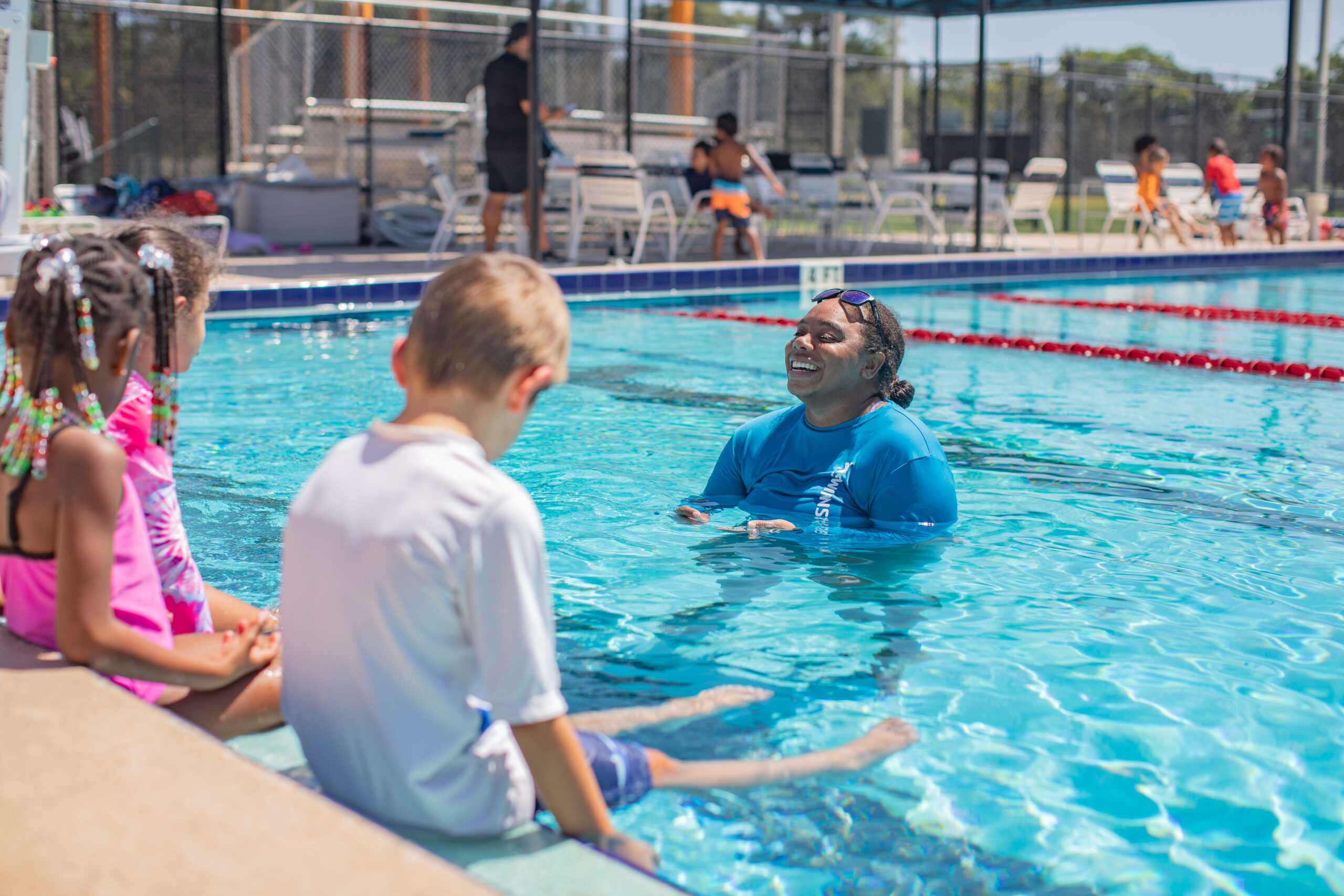 Woman in pool during swim lessons with children sitting on the edge of the pool surface