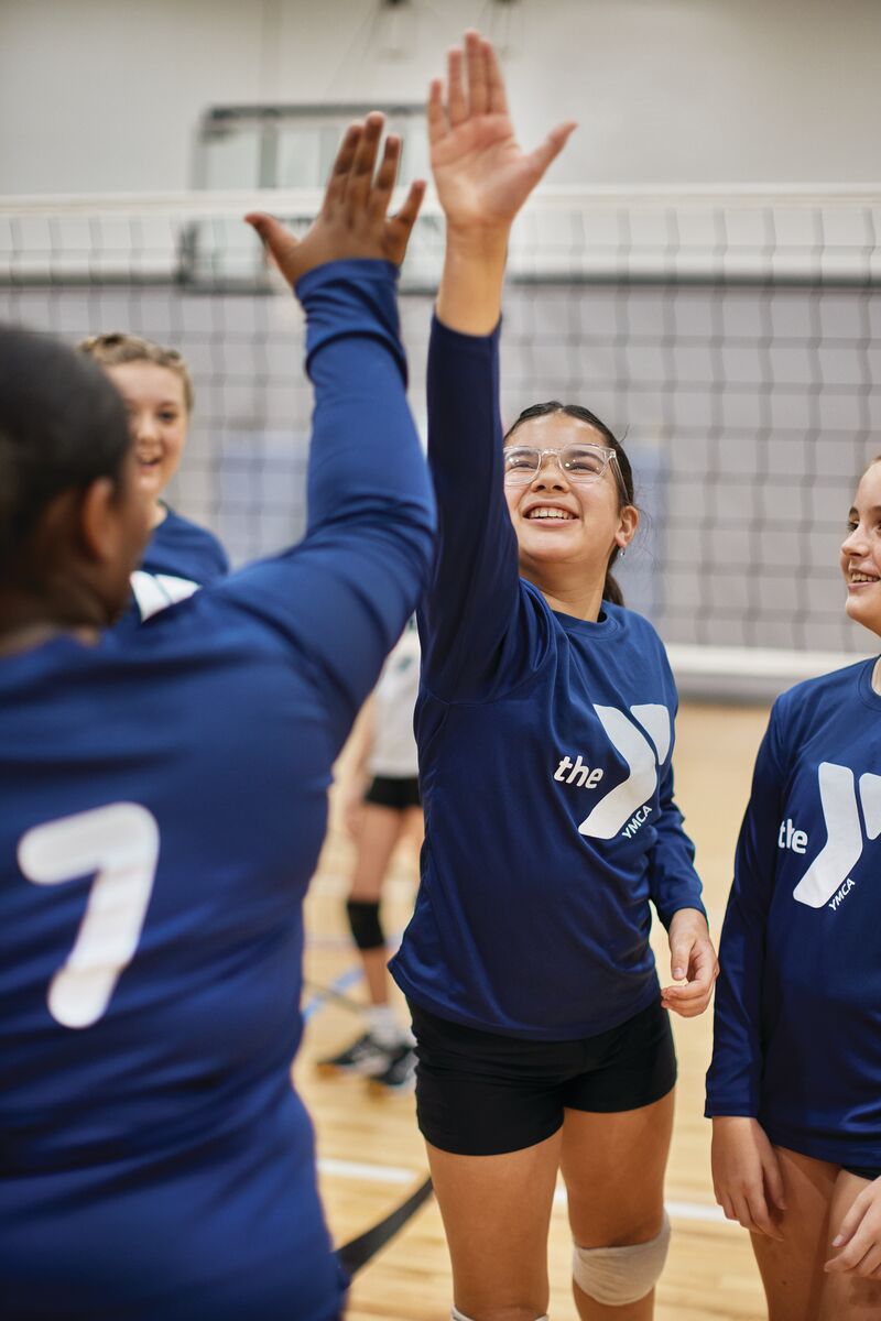 Girl vollyeball player high-fiving her fellow volleyball teammates on a volleyball court