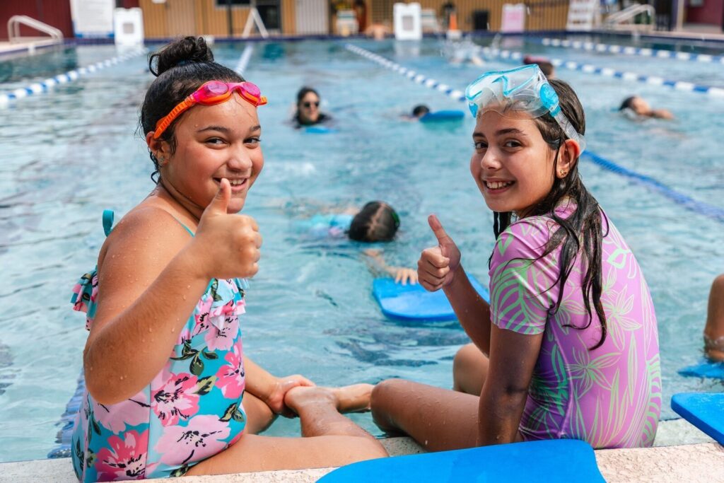 Two girls giving the thumbs up during their group swim lesson at the Lake Nona YMCA