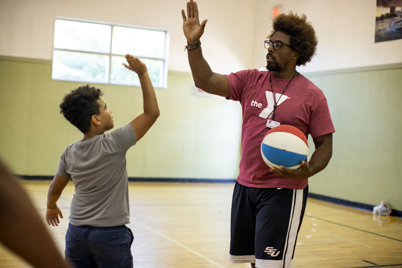 A camp counselor high-fiving a boy during holiday school break camp at the YMCA
