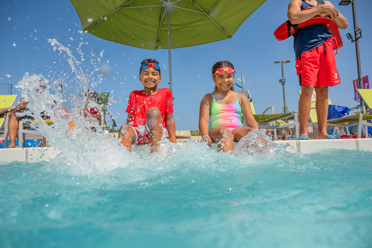 A boy and girl splashing their feet at the edge of the pool at the YMCA