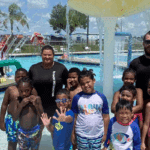 Kids and swim instructors standing under a mushroom waterfall at the Osceola County YMCA