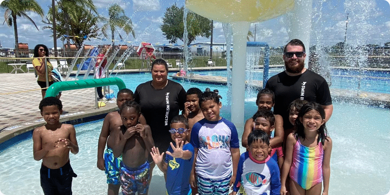 Kids and swim instructors standing under a mushroom waterfall at the Osceola County YMCA