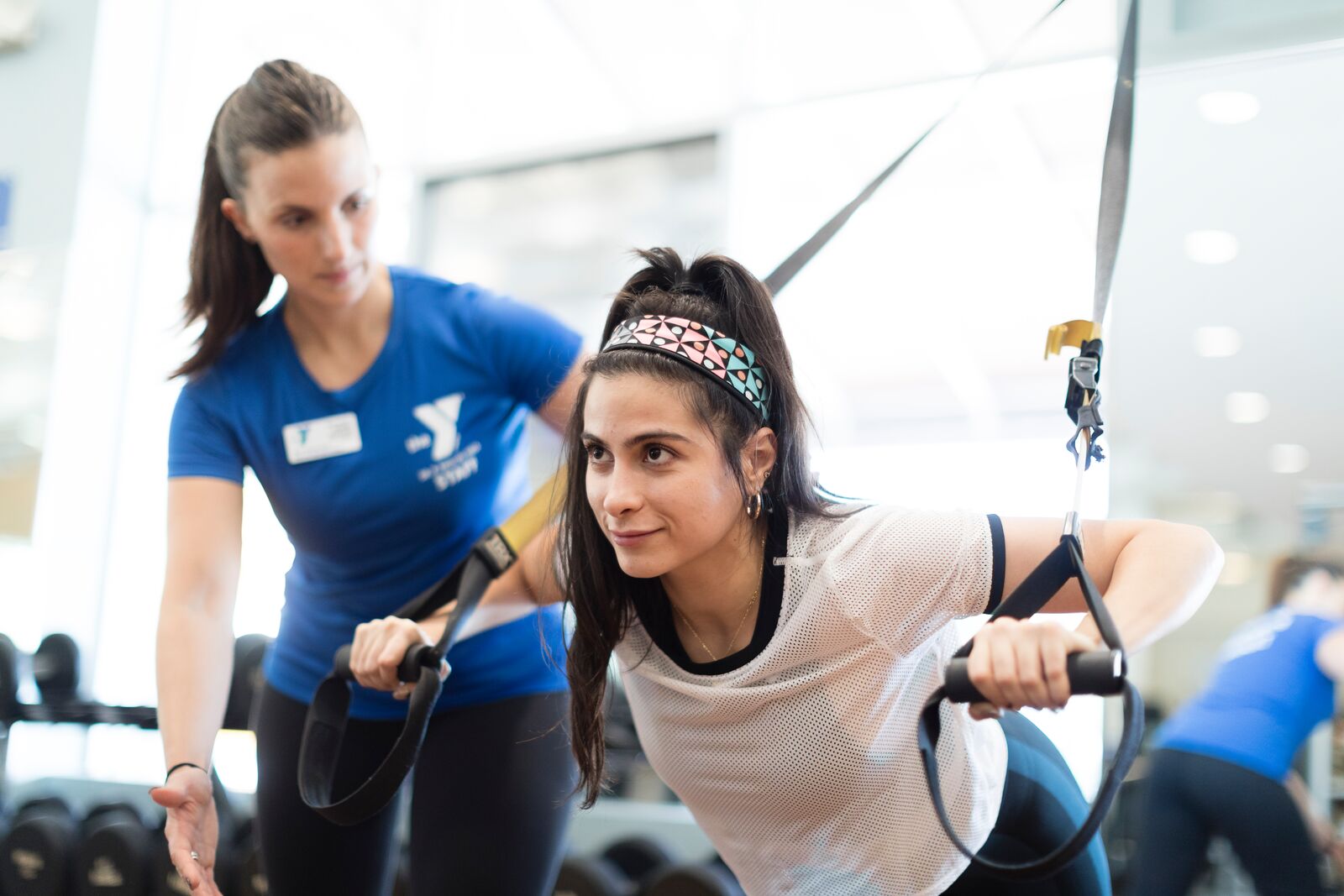 A young woman using the TRX suspension training system to workout with a personal trainer at the Y