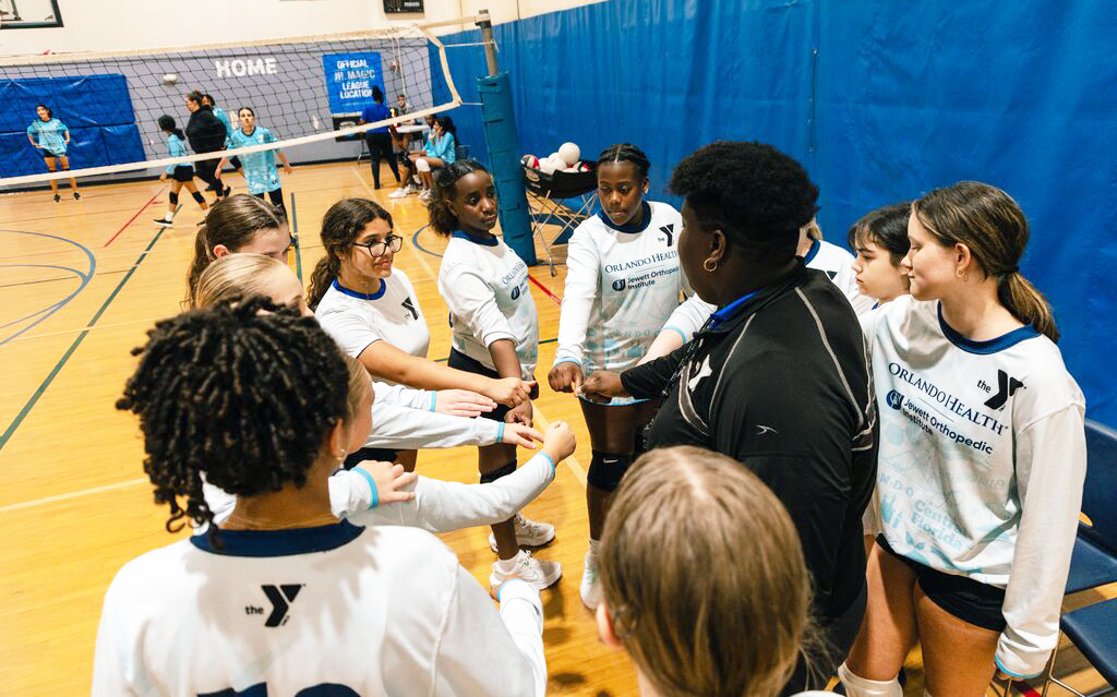 Girls in a huddle with their coach during a volleyball game at the YMCA