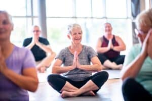 Woman sitting in Sukhasana, or Easy Pose, and smiling in group of Seniors in a meditation yoga class