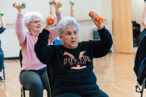 Seniors sitting in a chair doing an overhead press with dumbbells