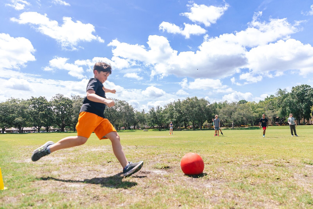 Boy swinging his leg to kick a ball on a large field during Summer Camp at the YMCA of Central Florida