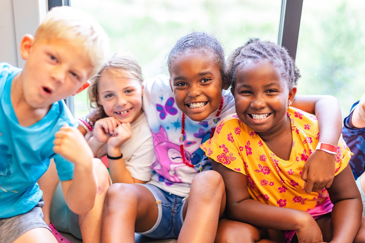 Four kids huddled laughing during summer camp at Leonard & Marjorie Williams YMCA